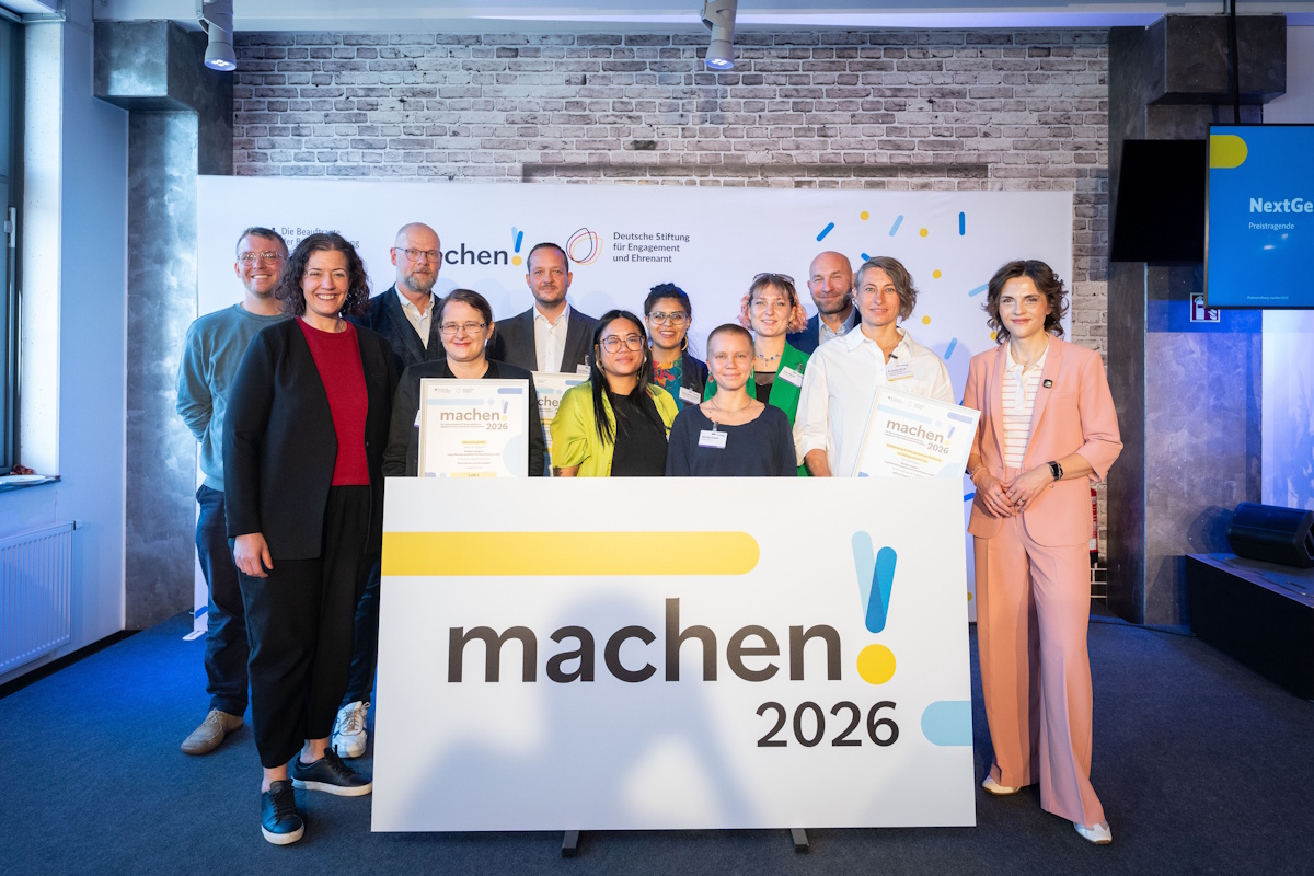 Momelino: Eine Gruppe von Menschen l&auml;chelt bei einer Preisverleihung vor einem Banner mit der Aufschrift machen! 2026 und h&auml;lt Urkunden in die Kamera.