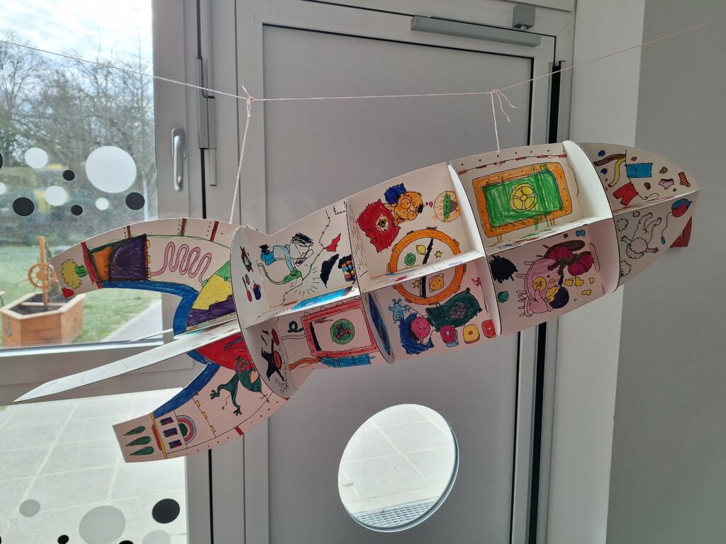 Momelino: Ein kreatives Kunstwerk eines Raumschiffs, das von Kindern im Momelino gestaltet wurde, h&auml;ngt in einem hellen Raum.